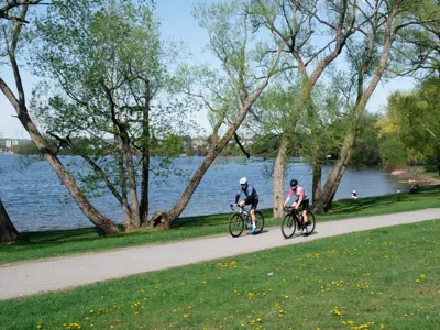 Two people riding their bikes on a gravel trail beside the water.